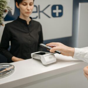 A woman witnesses a customer making a contactless payment using a smartphone at a service counter.